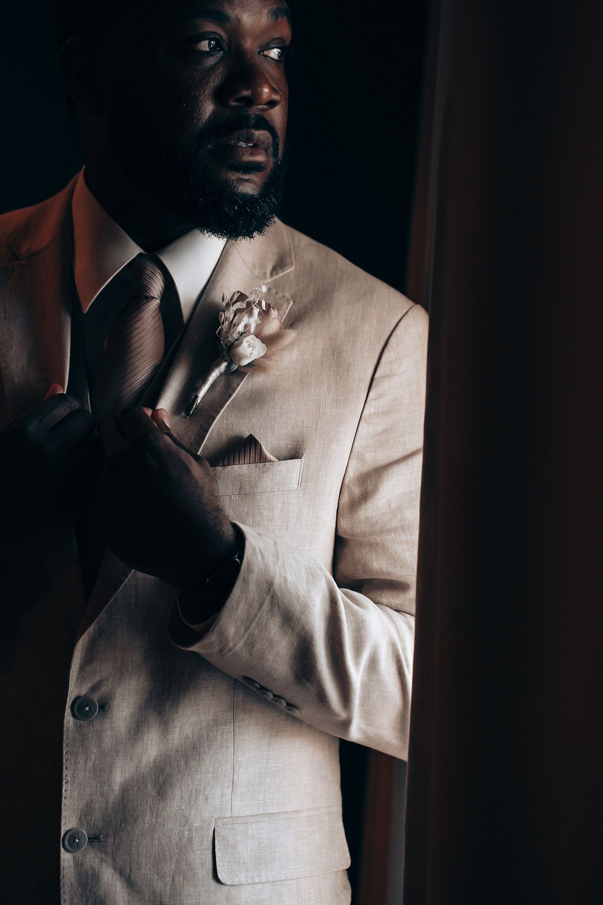 Artistic portrait of groom in cream suit with dramatic lighting and shadows.