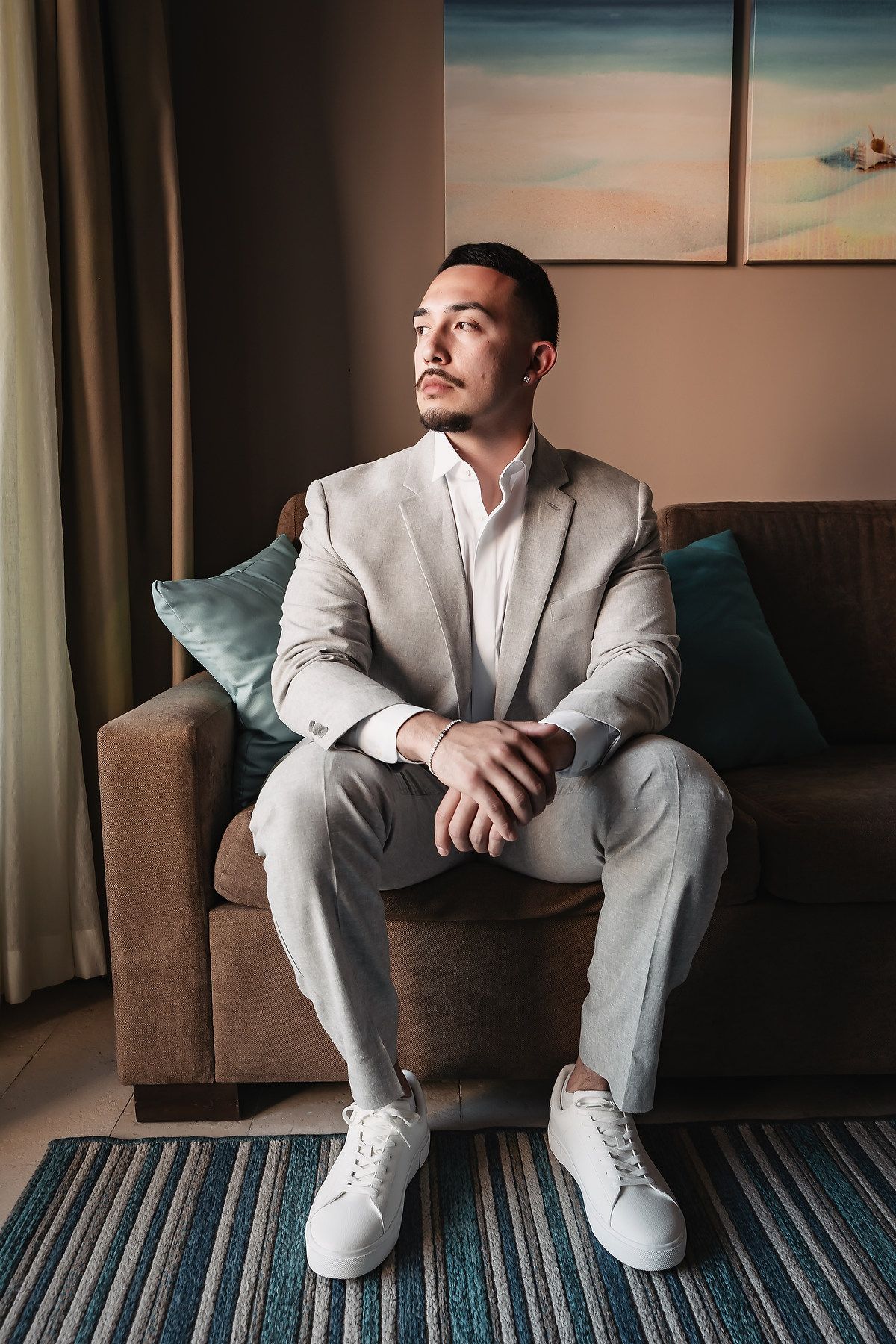 Person in light gray suit sitting thoughtfully on blue striped couch.