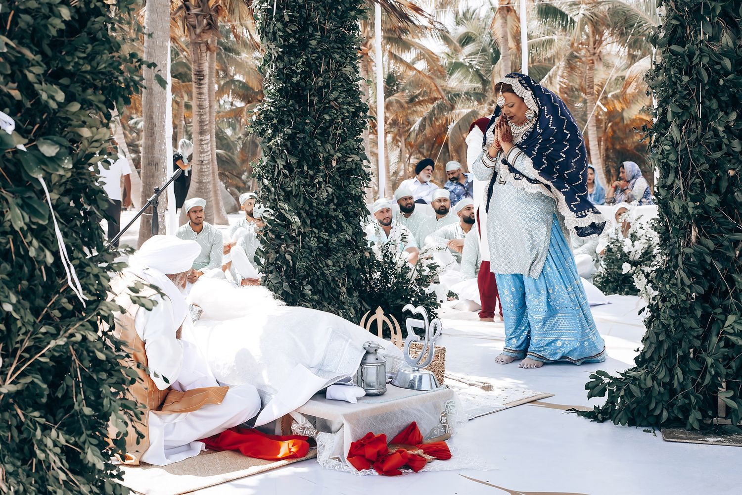 Cultural wedding ceremony with white and burgundy decor set against palm tree backdrop.