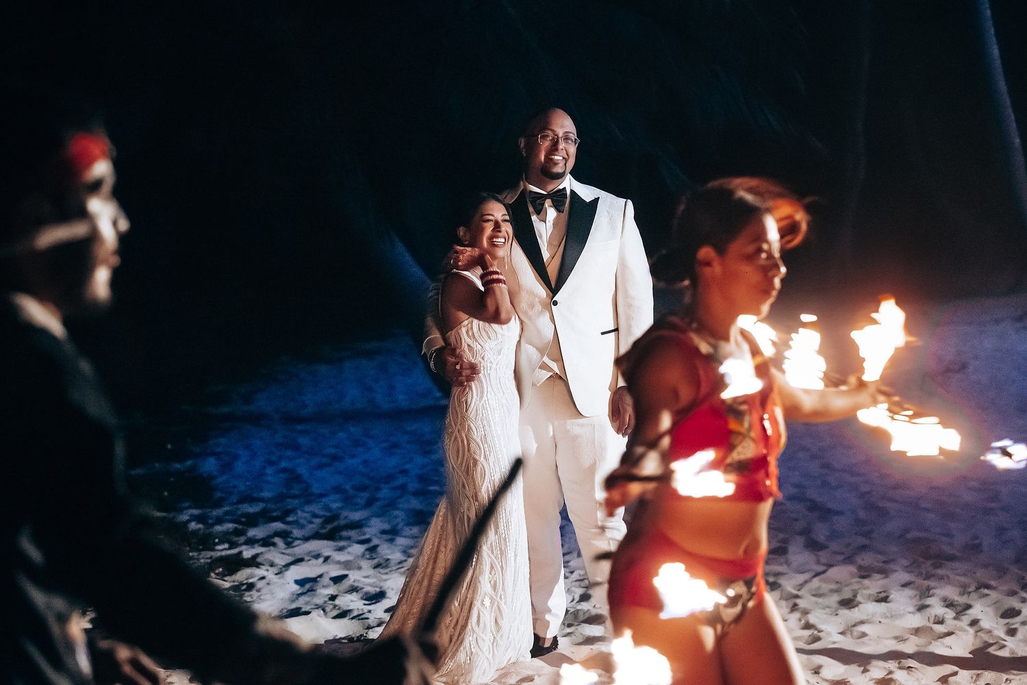 Wedding celebration on a beach with fire performers entertaining guests at night.