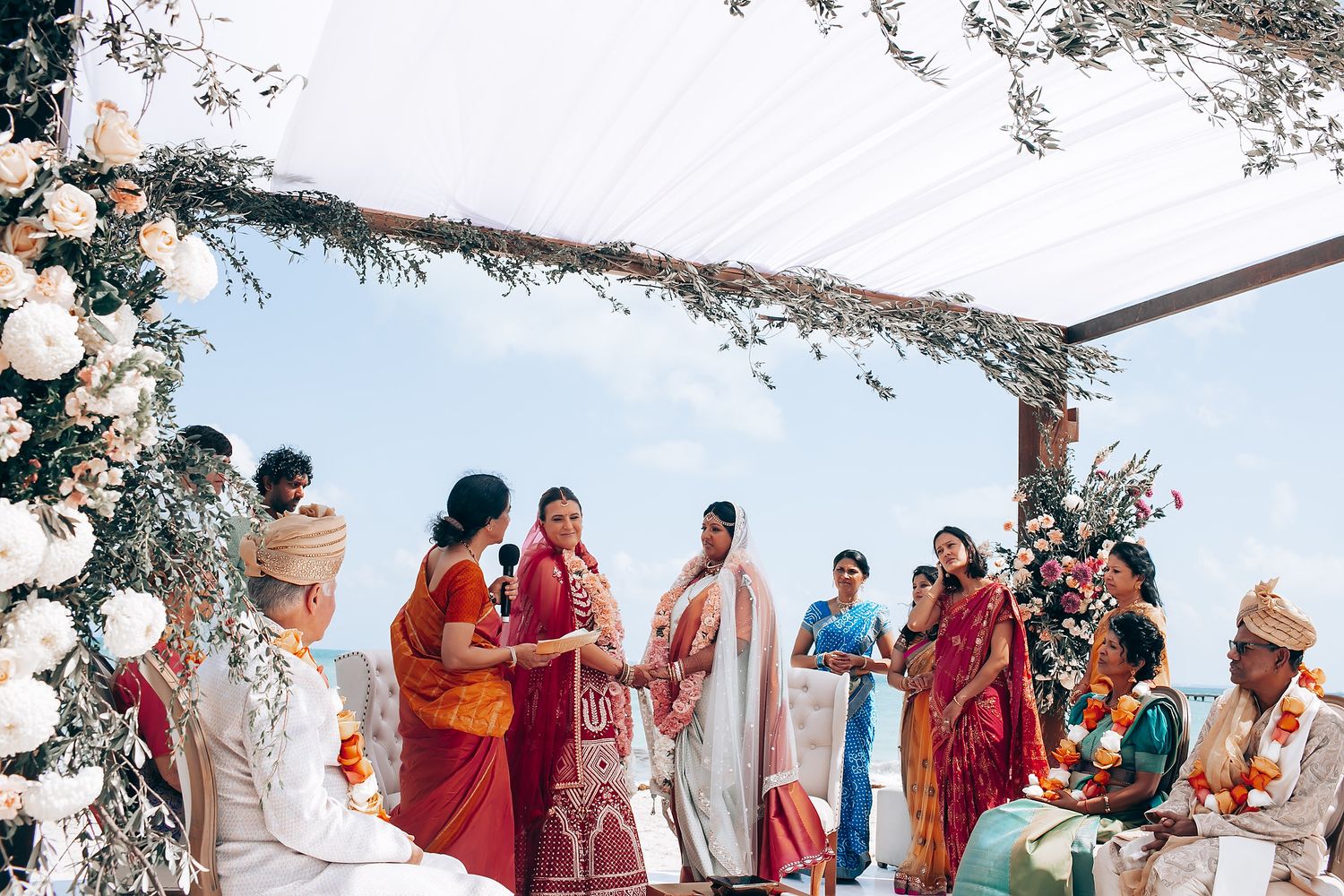 Beachside wedding ceremony with white canopy and floral arrangements overlooking turquoise waters.