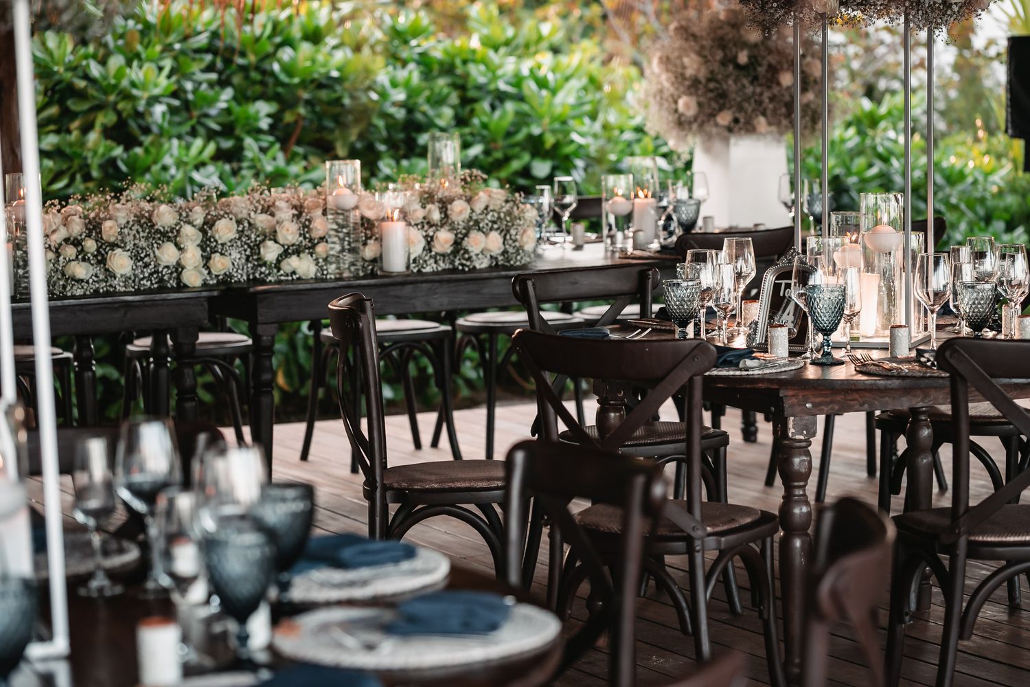 Elegant outdoor wedding reception with dark wood cross-back chairs and floral centerpieces.