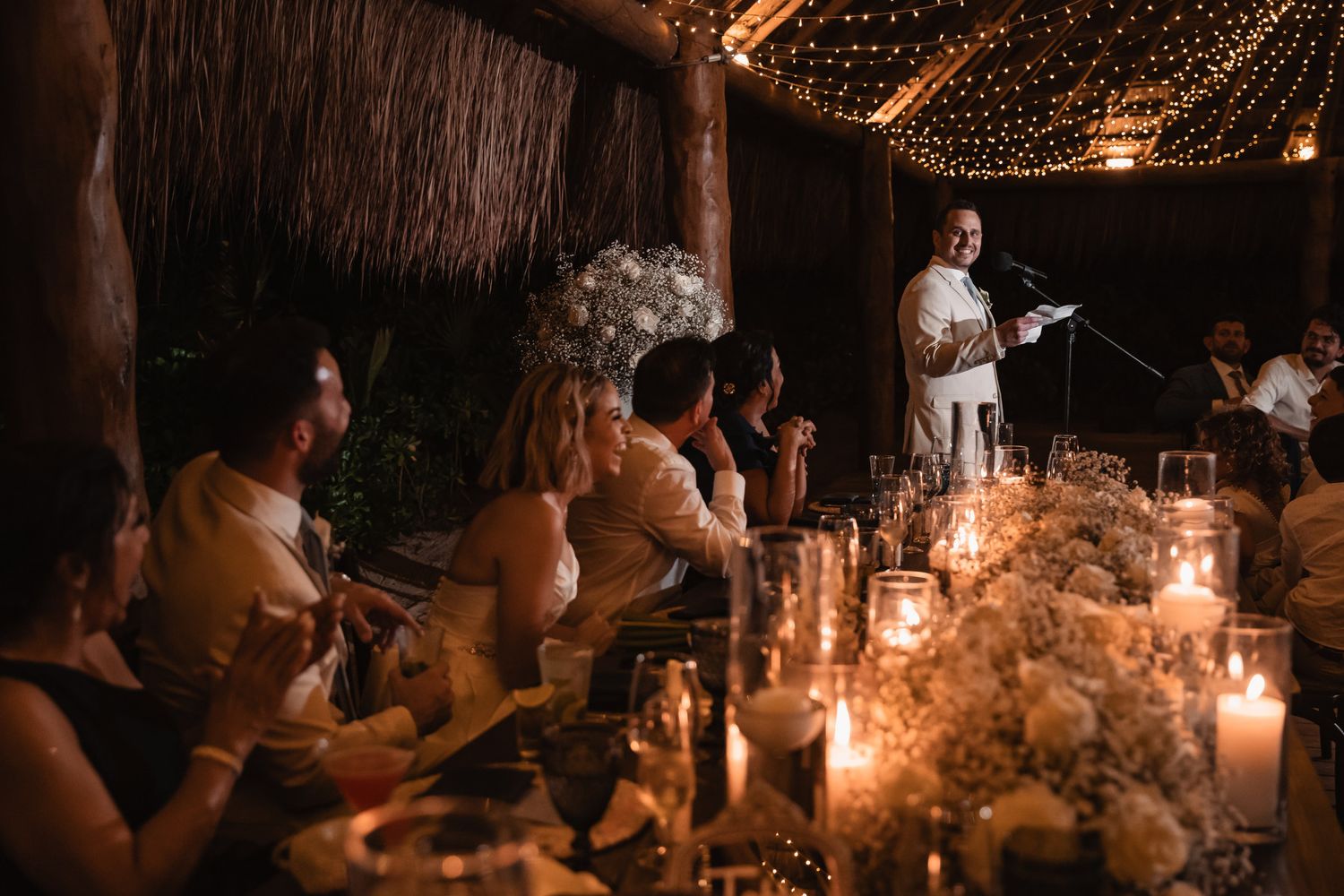 Wedding guest giving a heartfelt speech by candlelight at an intimate outdoor reception dinner.