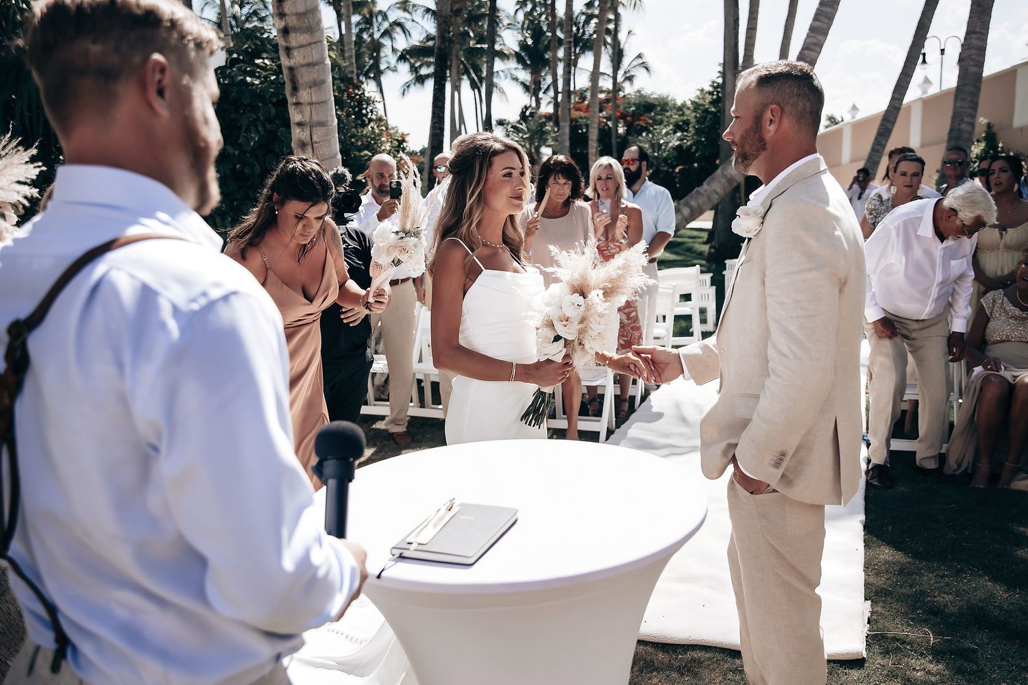 A couple in formal attire exchange vows at an outdoor wedding ceremony.