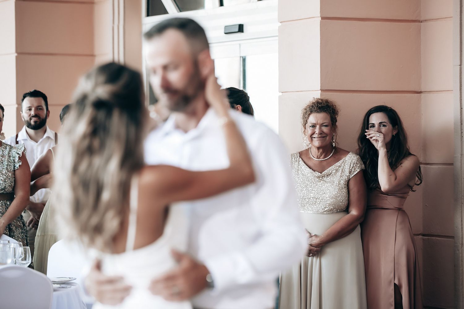 A bride and groom embracing at their wedding ceremony with guests in the background.