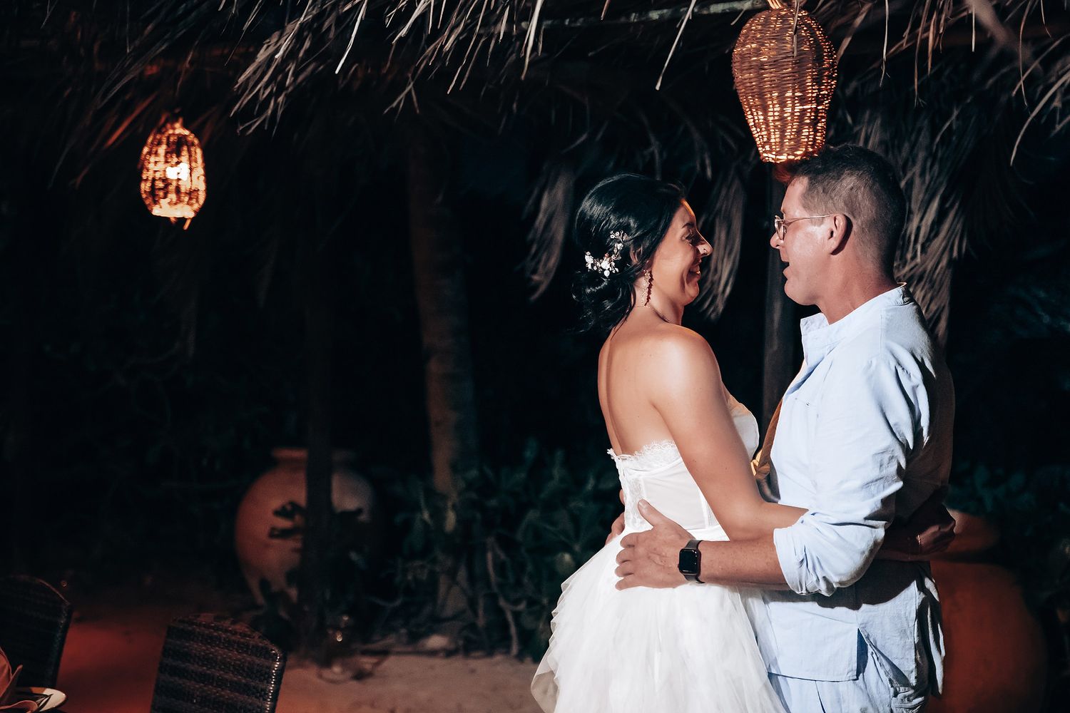 A couple dances together under twinkling lights at their tropical wedding reception.