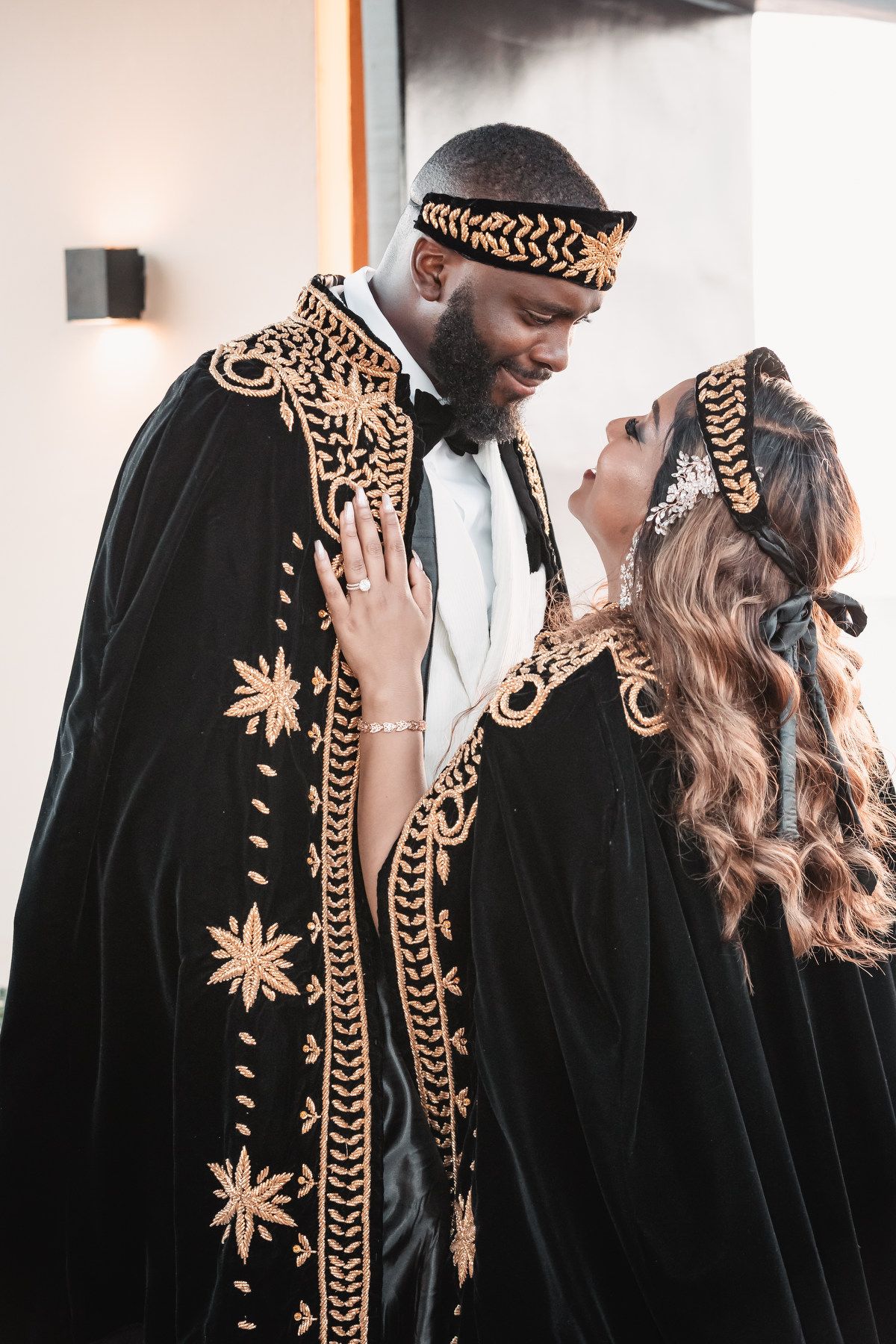 Couple in elegant black and gold embroidered traditional robes sharing a romantic moment during their cultural wedding ceremony.