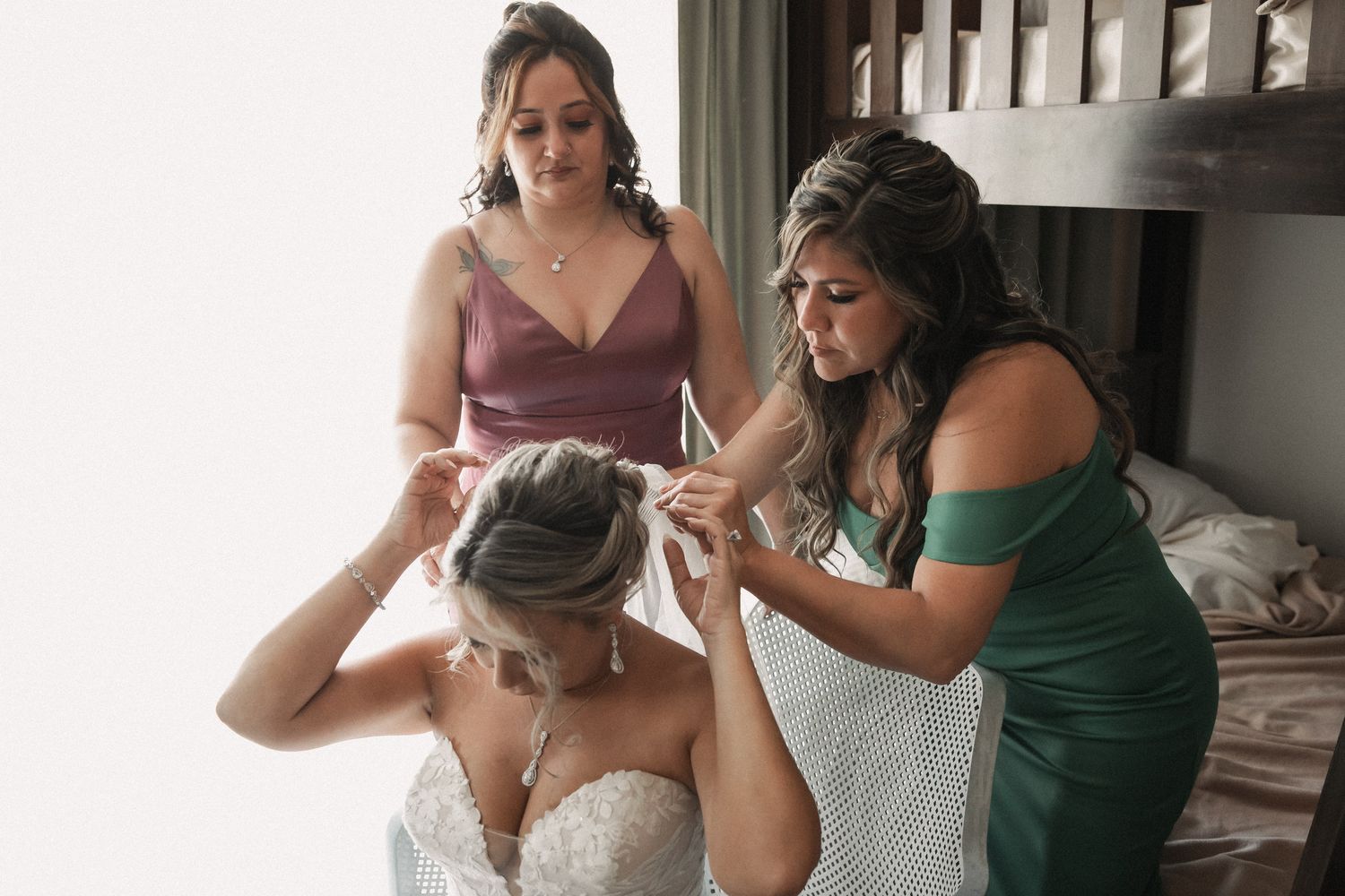 Bridesmaids helping bride with wedding dress details in a bright room before the ceremony.