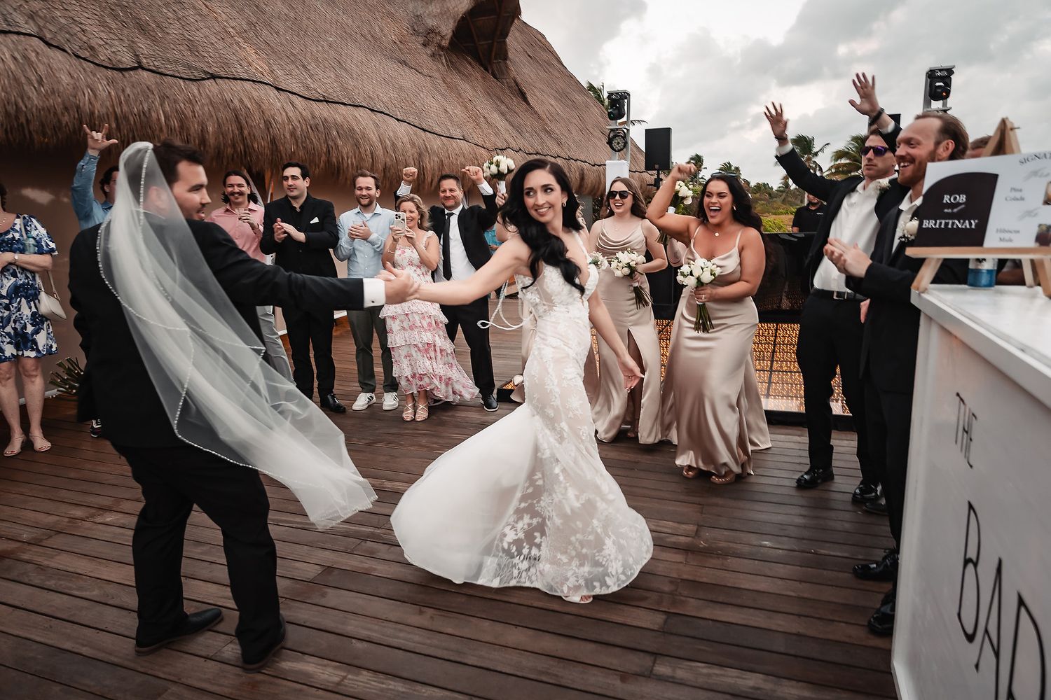 Bride and groom dancing joyfully at outdoor wedding reception with bridesmaids and guests celebrating in background.