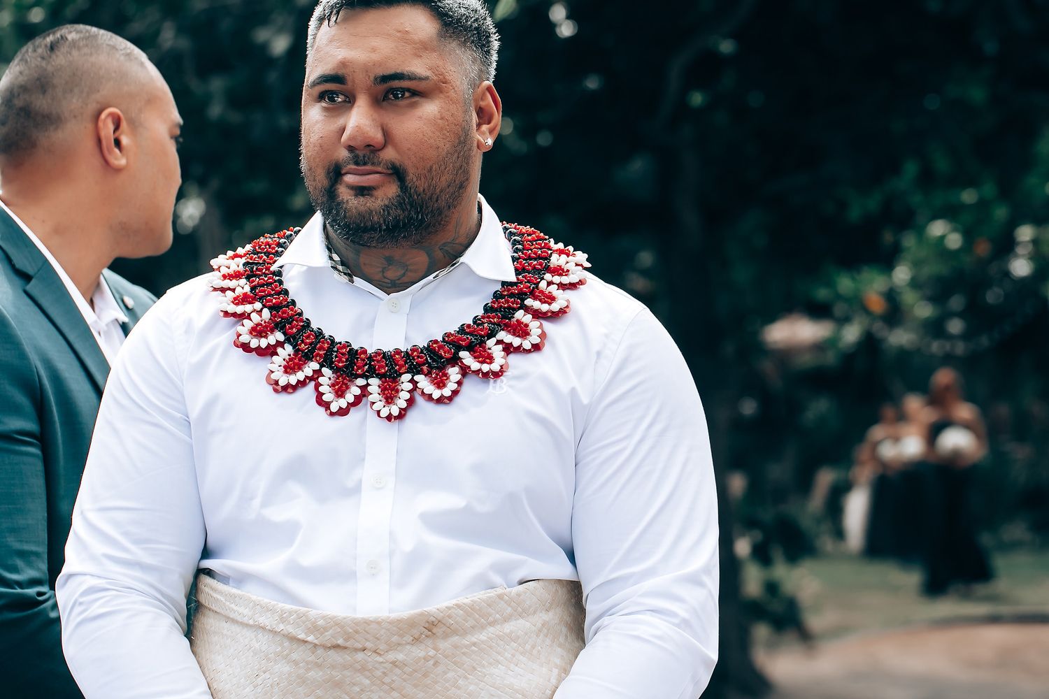 A person in a white shirt with red beaded necklace smiles during an outdoor celebration.