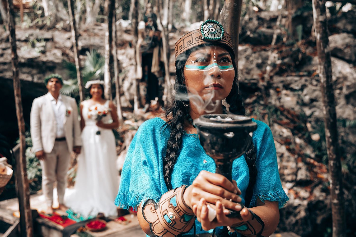 Person in turquoise traditional dress performs ceremonial ritual during outdoor wedding.