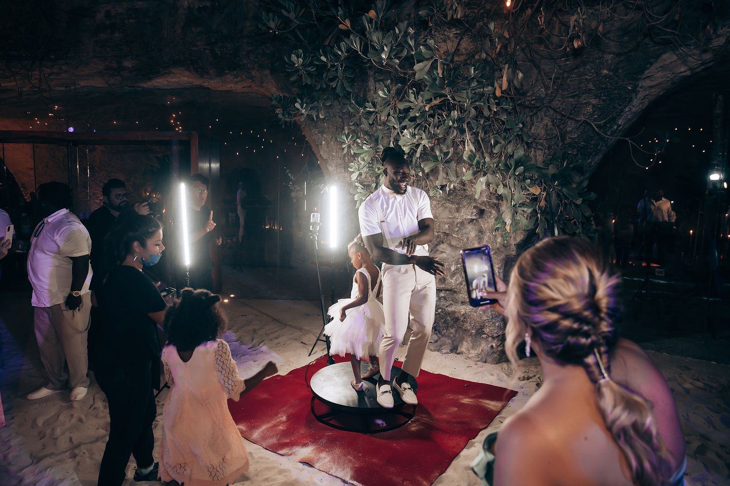 Wedding guests dance and celebrate on a dark dance floor illuminated by spotlights during an evening reception.