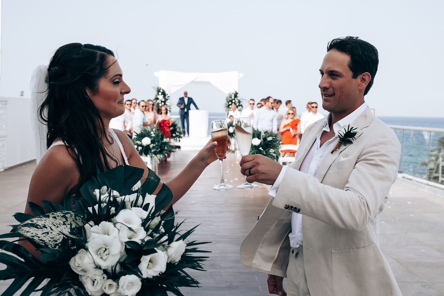 Newlyweds share a celebratory toast on an outdoor terrace with floral arrangements.