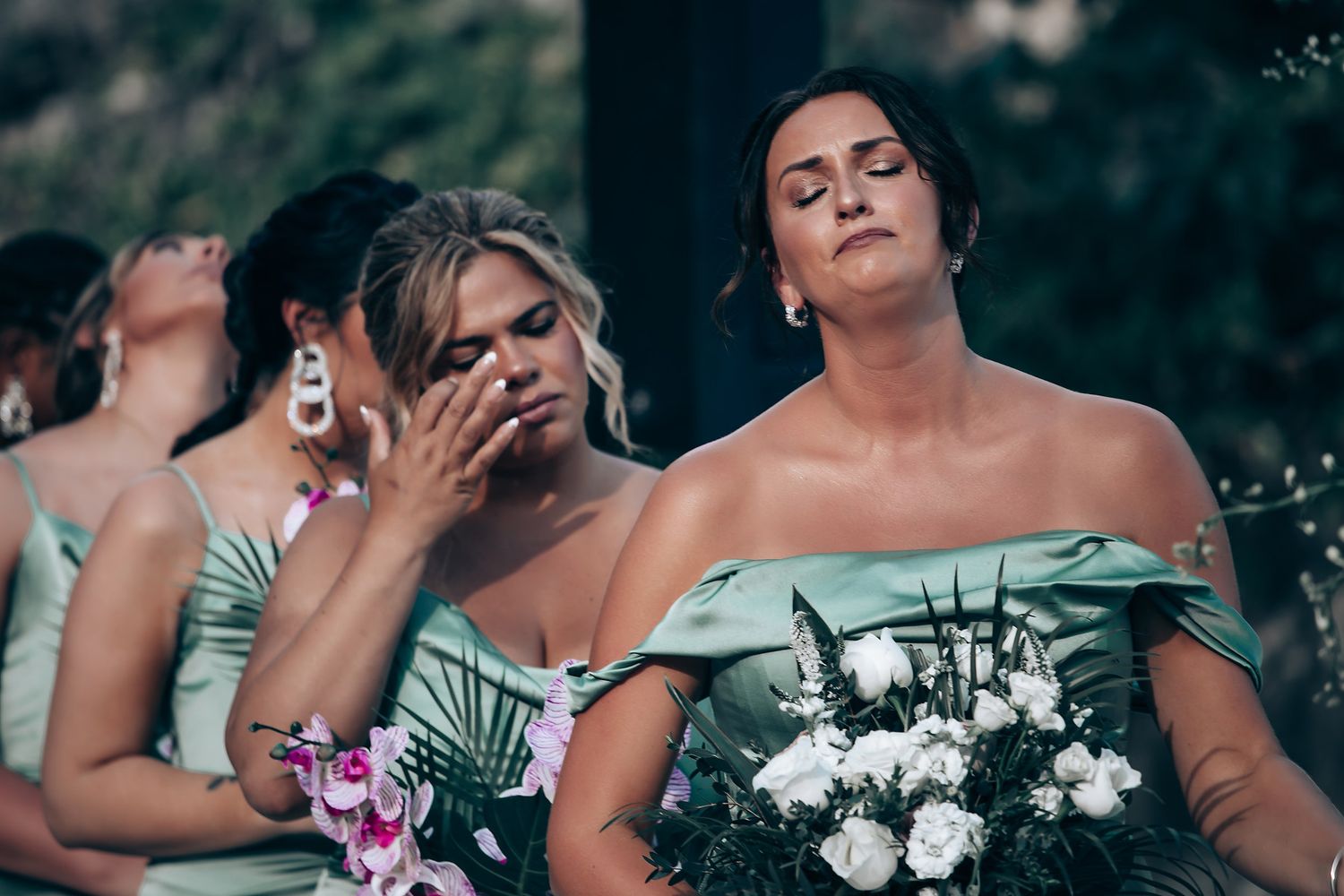 Bridesmaids in strapless sage green dresses share an emotional moment during wedding photos.