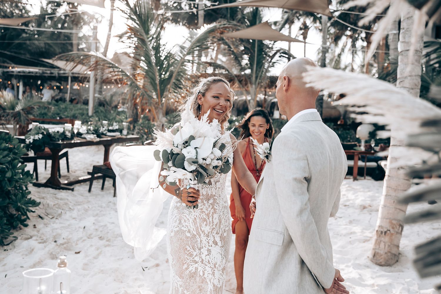 Intimate beach wedding ceremony under palm trees with white floral decorations.