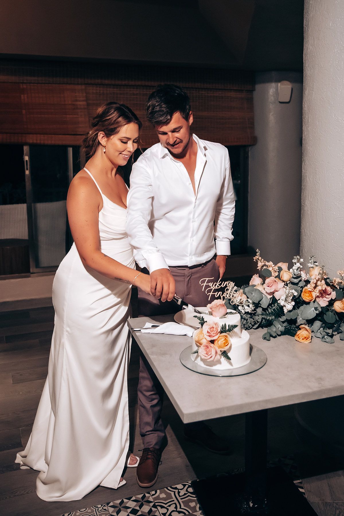 A couple cutting their wedding cake together at an elegant indoor reception with floral decorations.