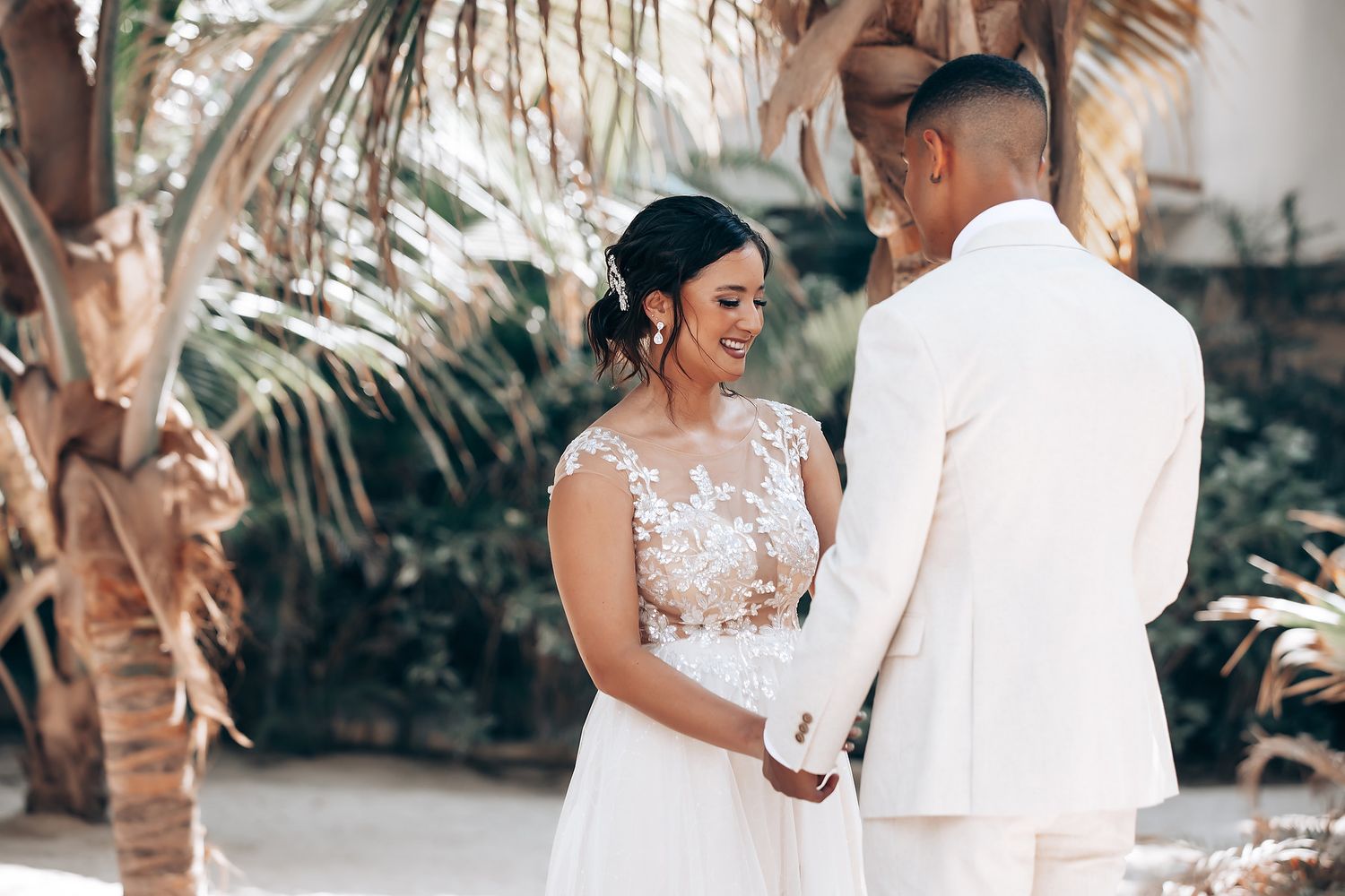 A romantic wedding photoshoot takes place among swaying palm trees on a sunny beach.