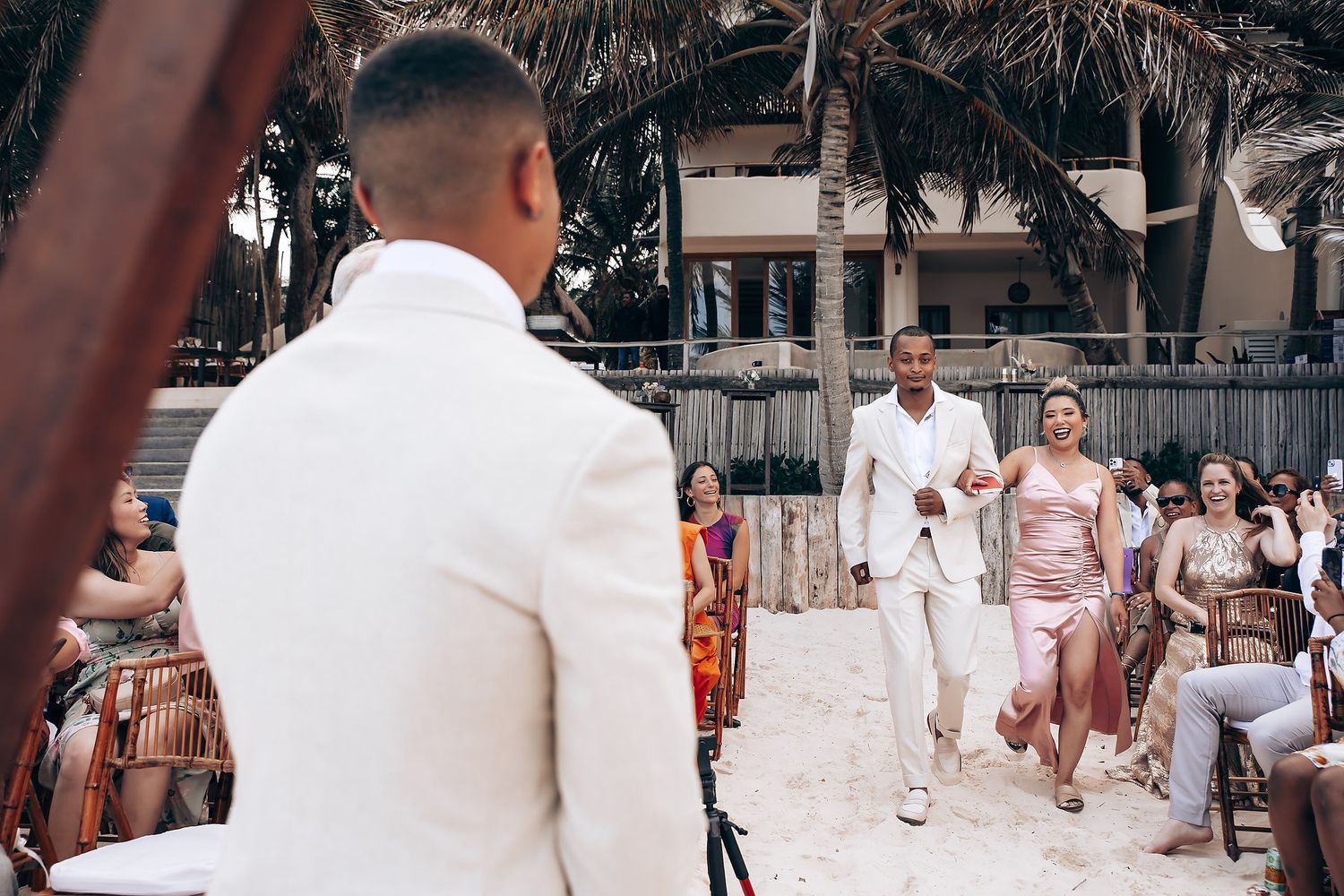 Guests seated at an outdoor beach wedding reception under palm trees.