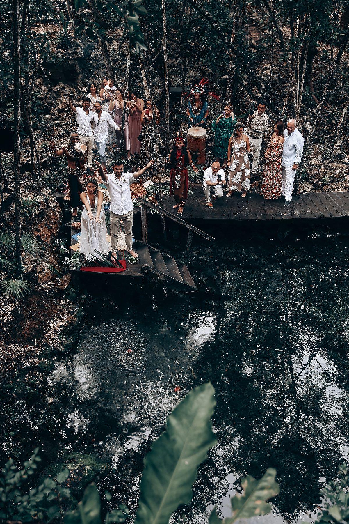 A group dressed in white stands together on a rustic wooden platform in a forest setting.