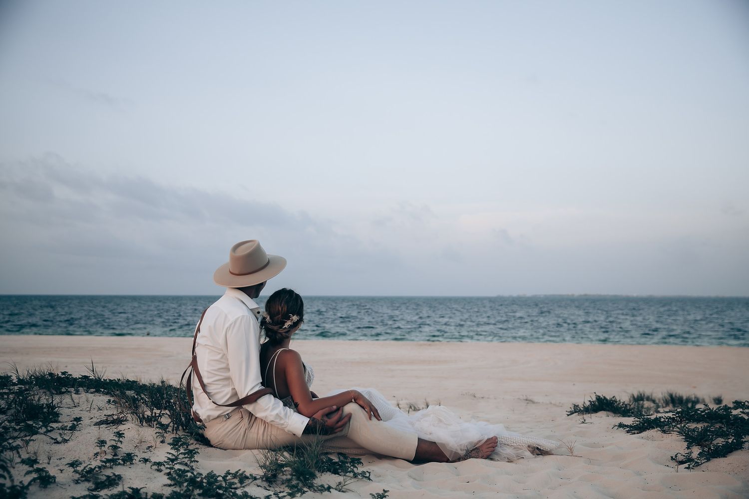 Couple enjoying a romantic moment on a sandy beach with ocean views at sunset.