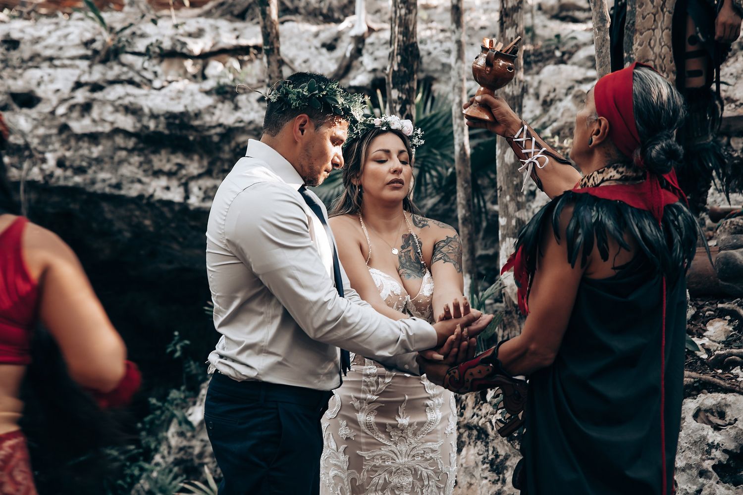 Wedding ceremony participants gather around a rustic wooden table in a forest setting.