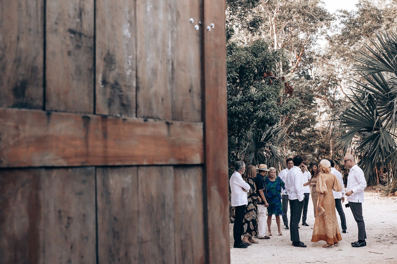 Rustic wooden wall backdrop at an outdoor event with guests mingling in the background.