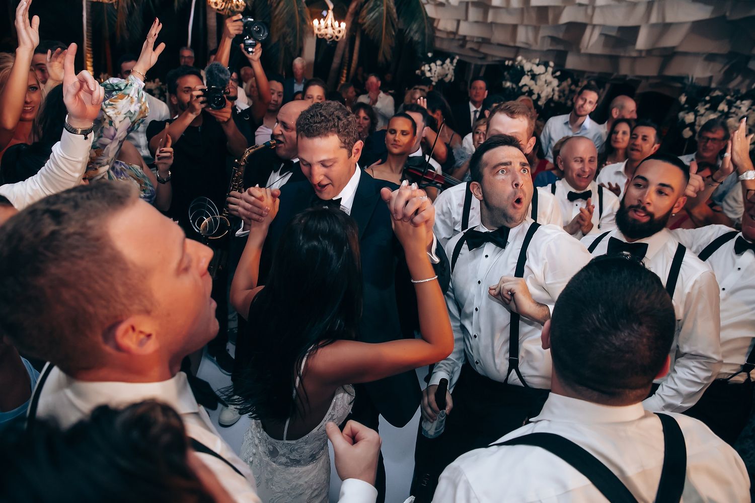 Energetic wedding reception dance party with crowd in formal attire.