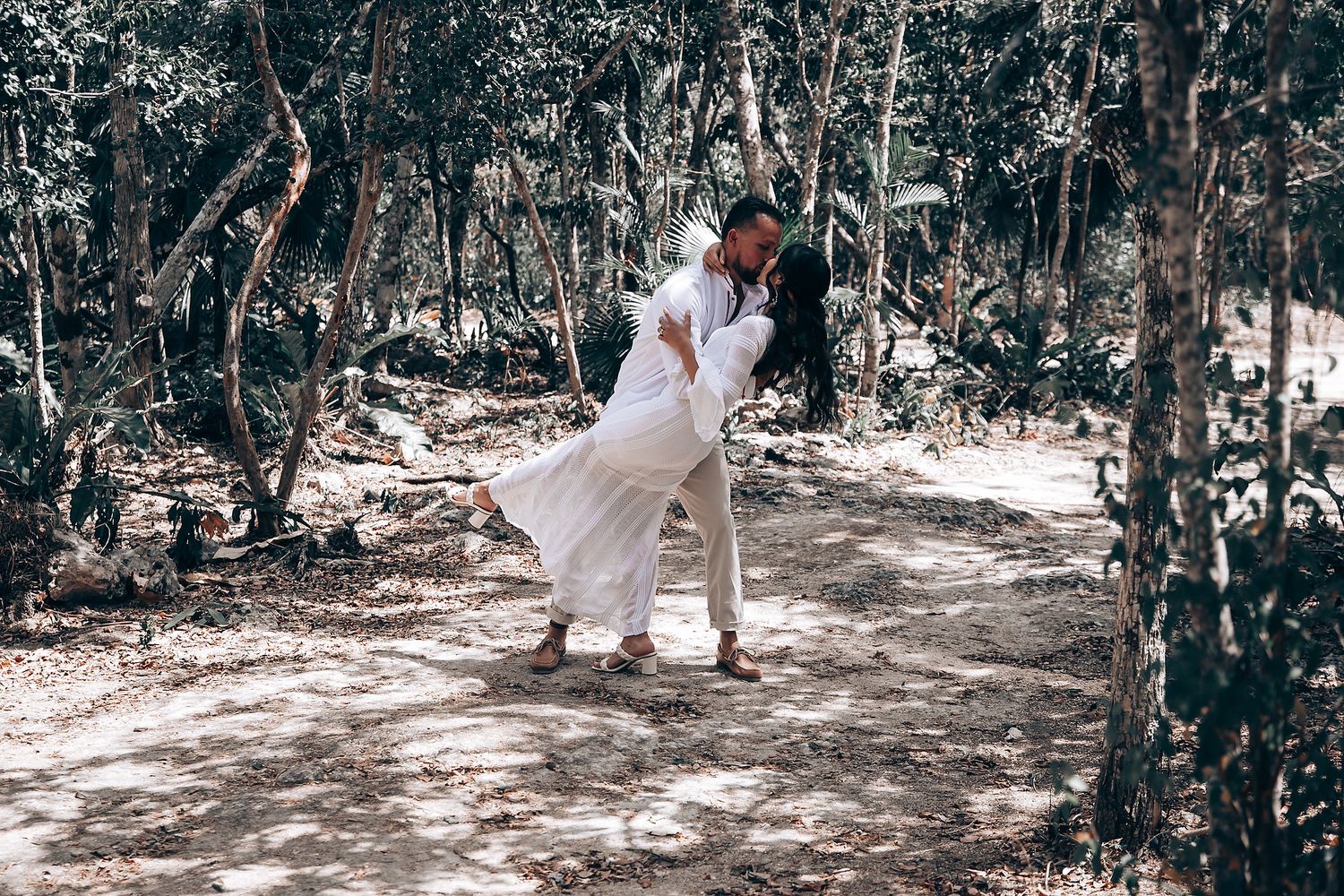 Outdoor wedding gathering in a sunlit wooded area with natural decor.