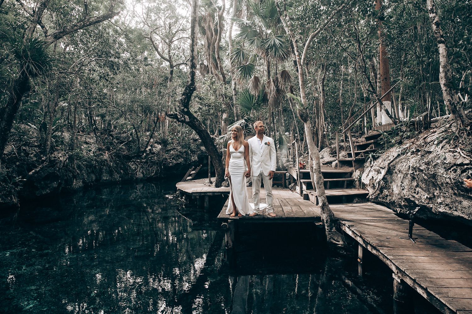A wooden boardwalk extends through a mystical forest landscape with reflective water.