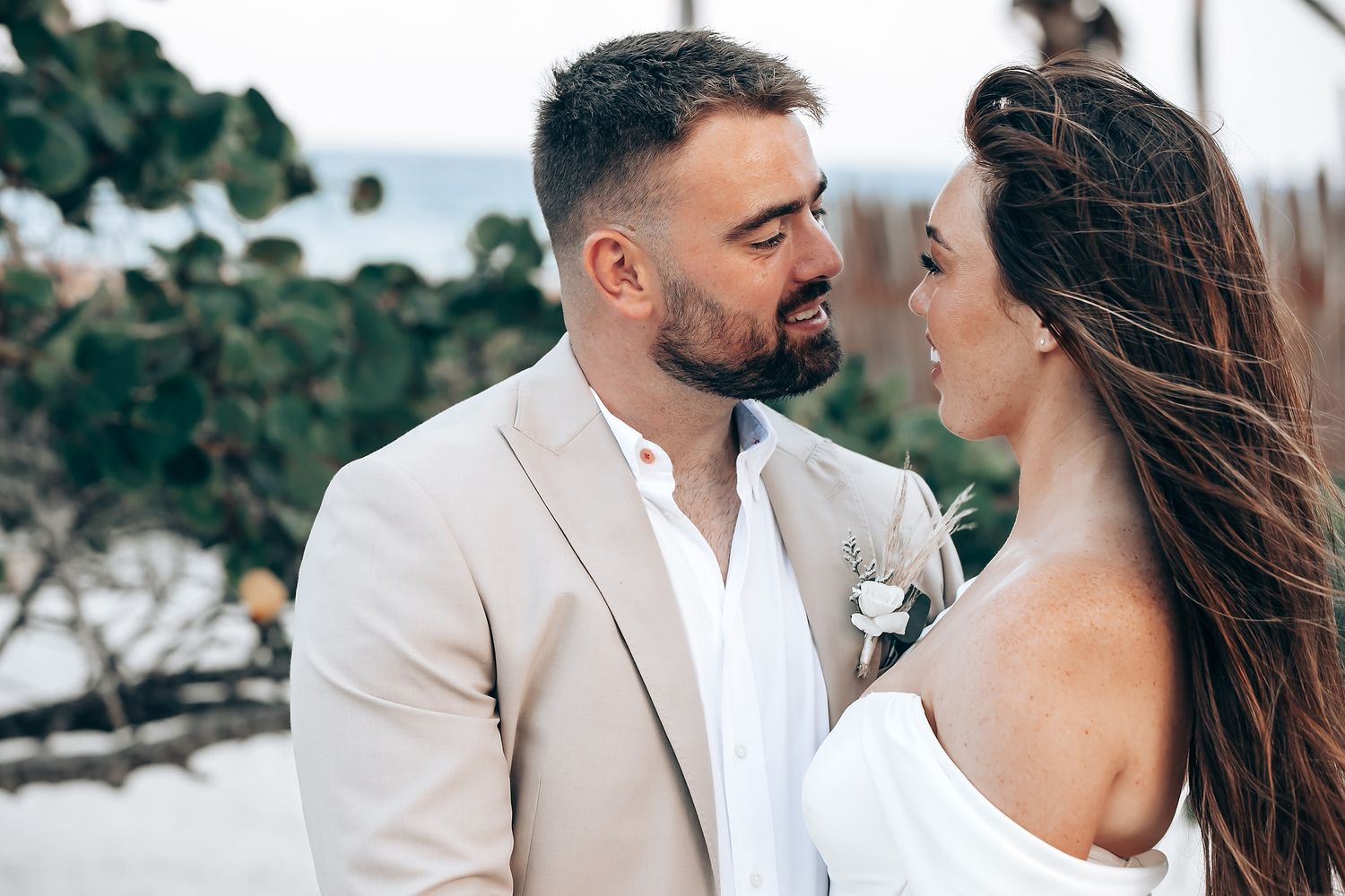 A romantic couple shares intimate moments in a coastal setting wearing coordinated white and beige outfits.