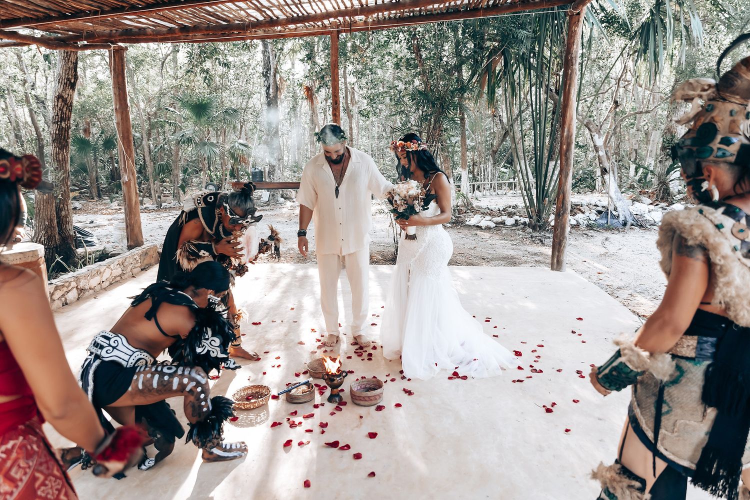 A wedding ceremony under a rustic wooden canopy decorated with rose petals.