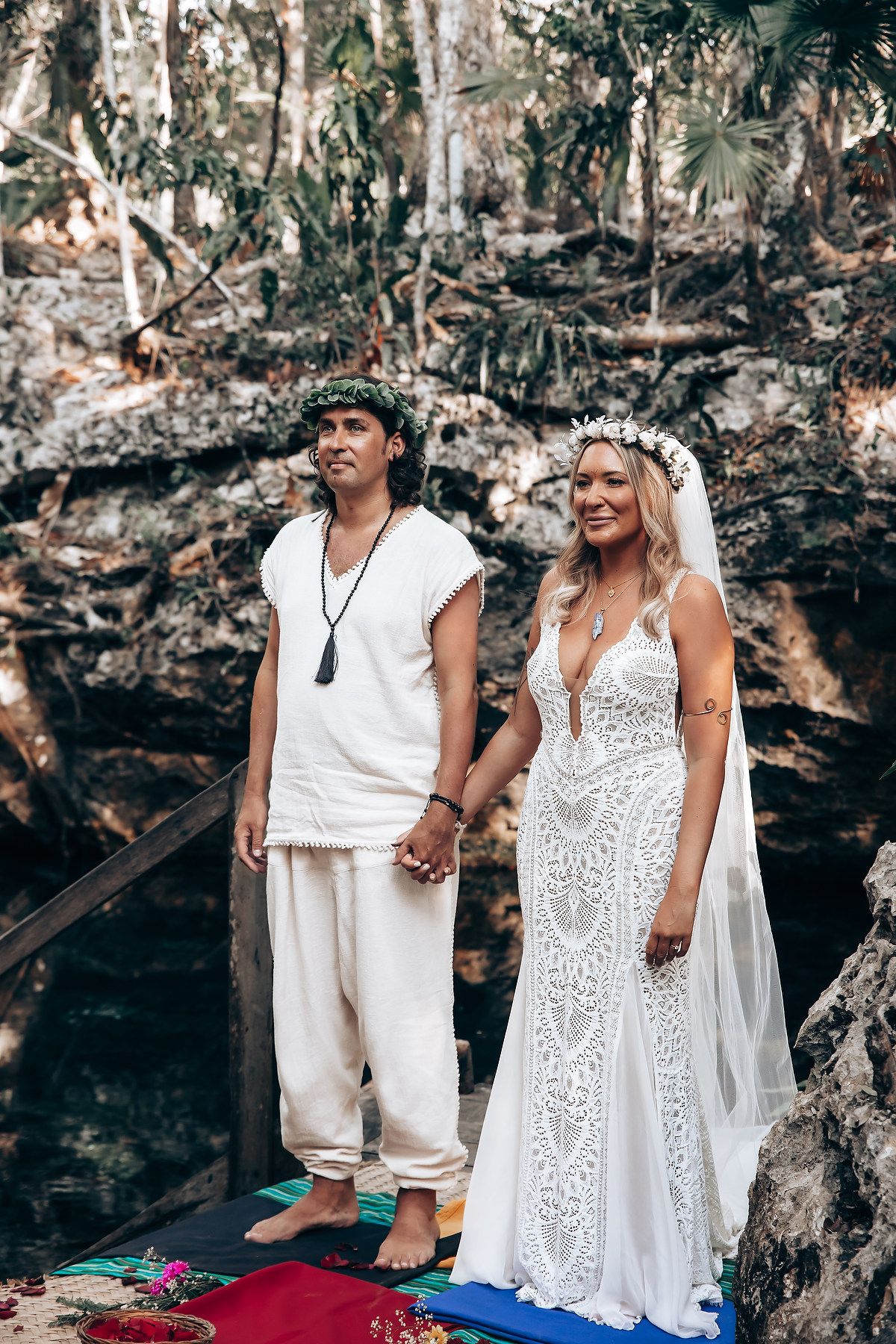 A couple in white outfits poses together against a rocky backdrop in a romantic outdoor photoshoot.