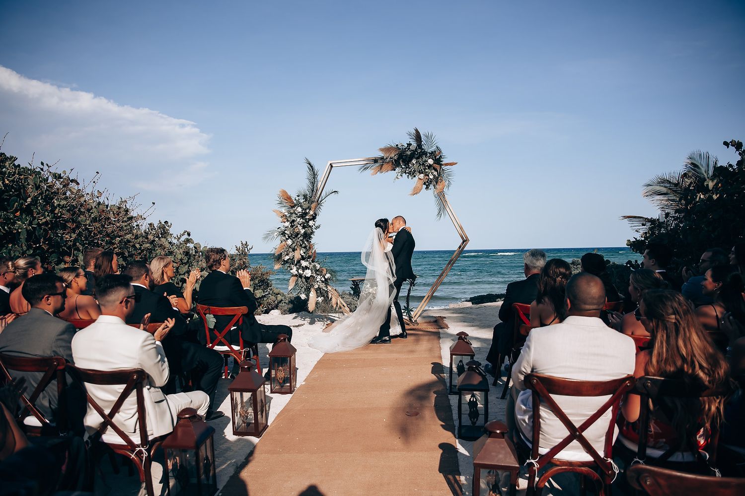 Wedding guests seated in white chairs at an outdoor beachfront ceremony.