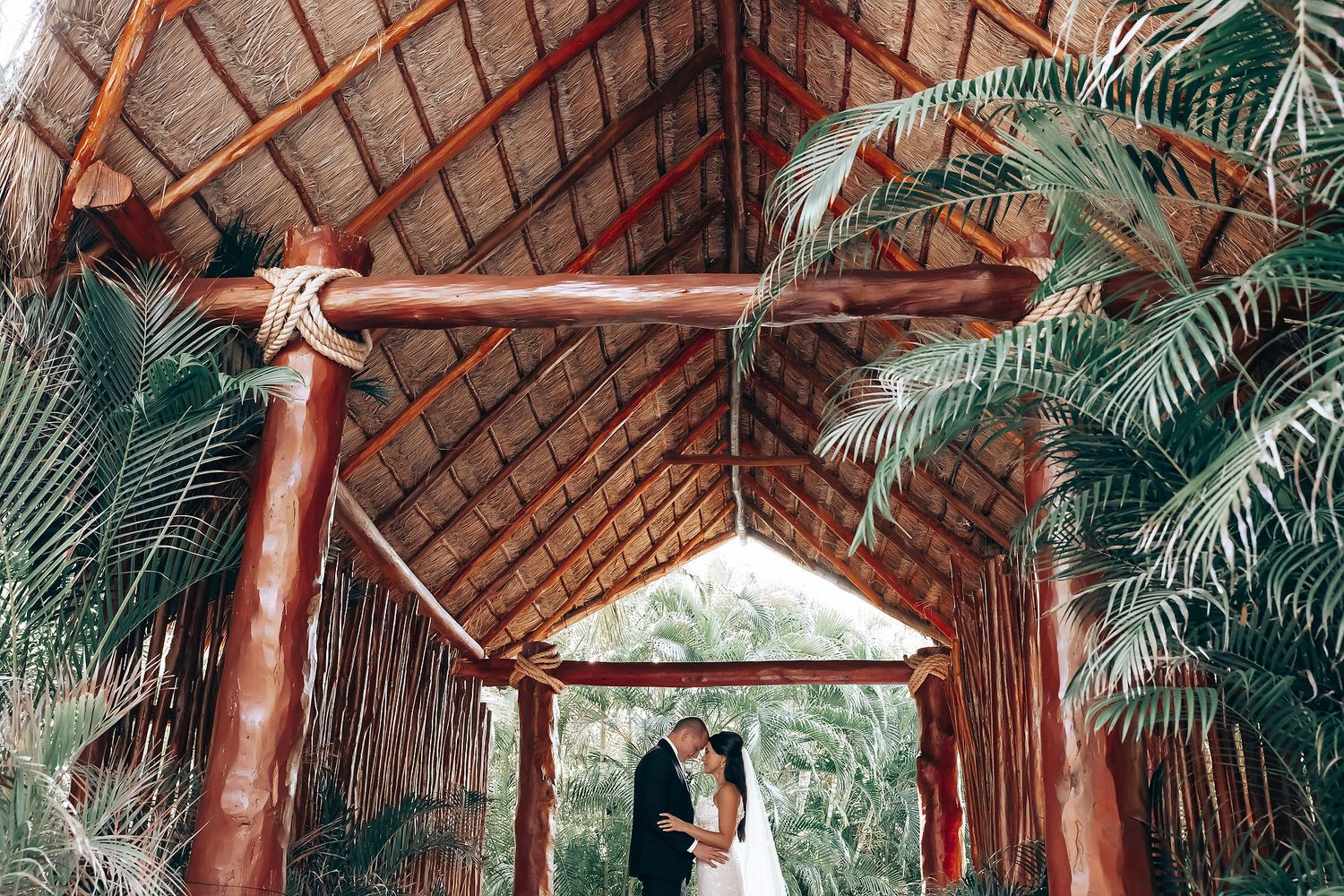 Rustic wooden beams and palm fronds create a tropical wedding ceremony venue setting.