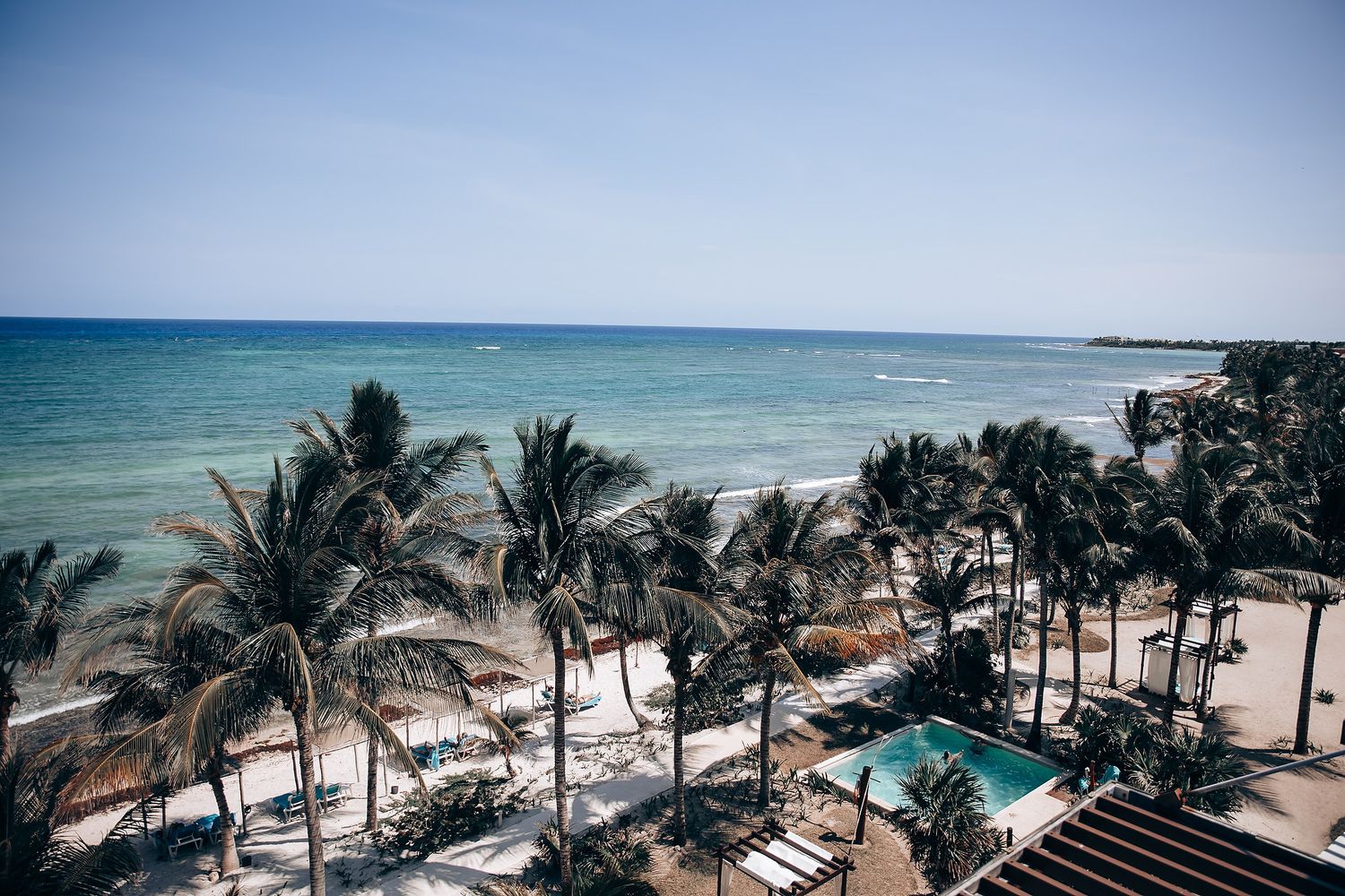 Aerial panoramic view of a tropical beach with palm trees and turquoise ocean waters stretching along the coastline.