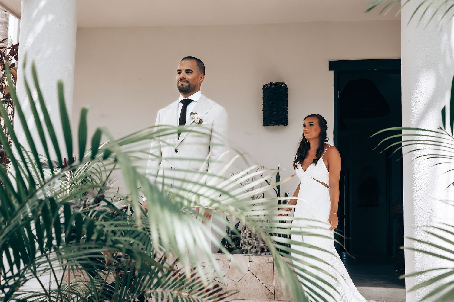 Wedding party celebrates in a tropical indoor venue decorated with palm leaves and white decor.
