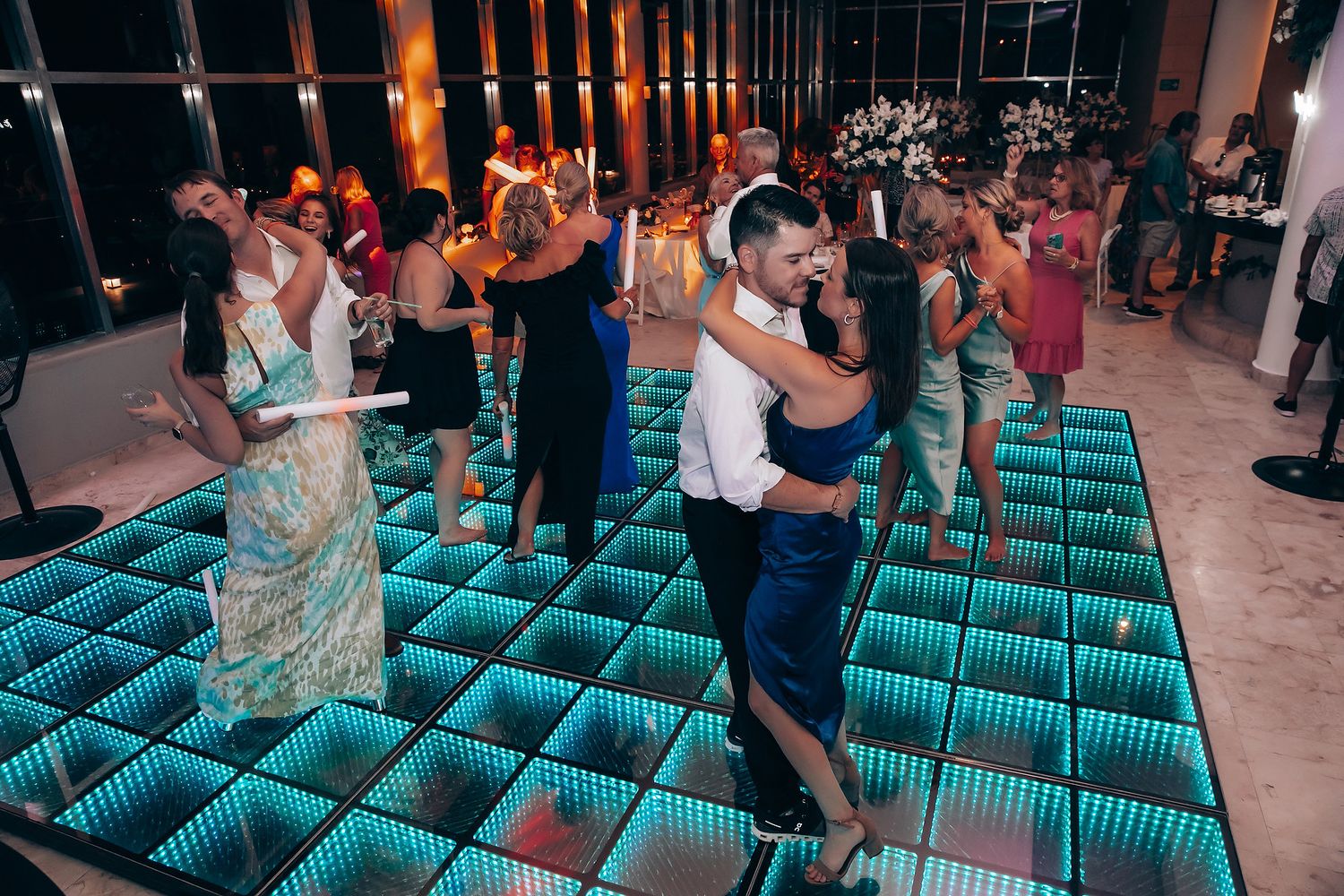 Wedding guests dance on an illuminated blue LED dance floor during reception celebrations.