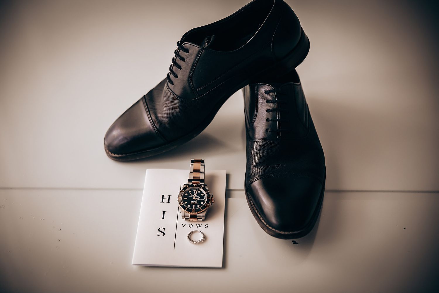 Elegant brown leather dress shoes and a watch displayed on a white surface with vignette lighting effect.