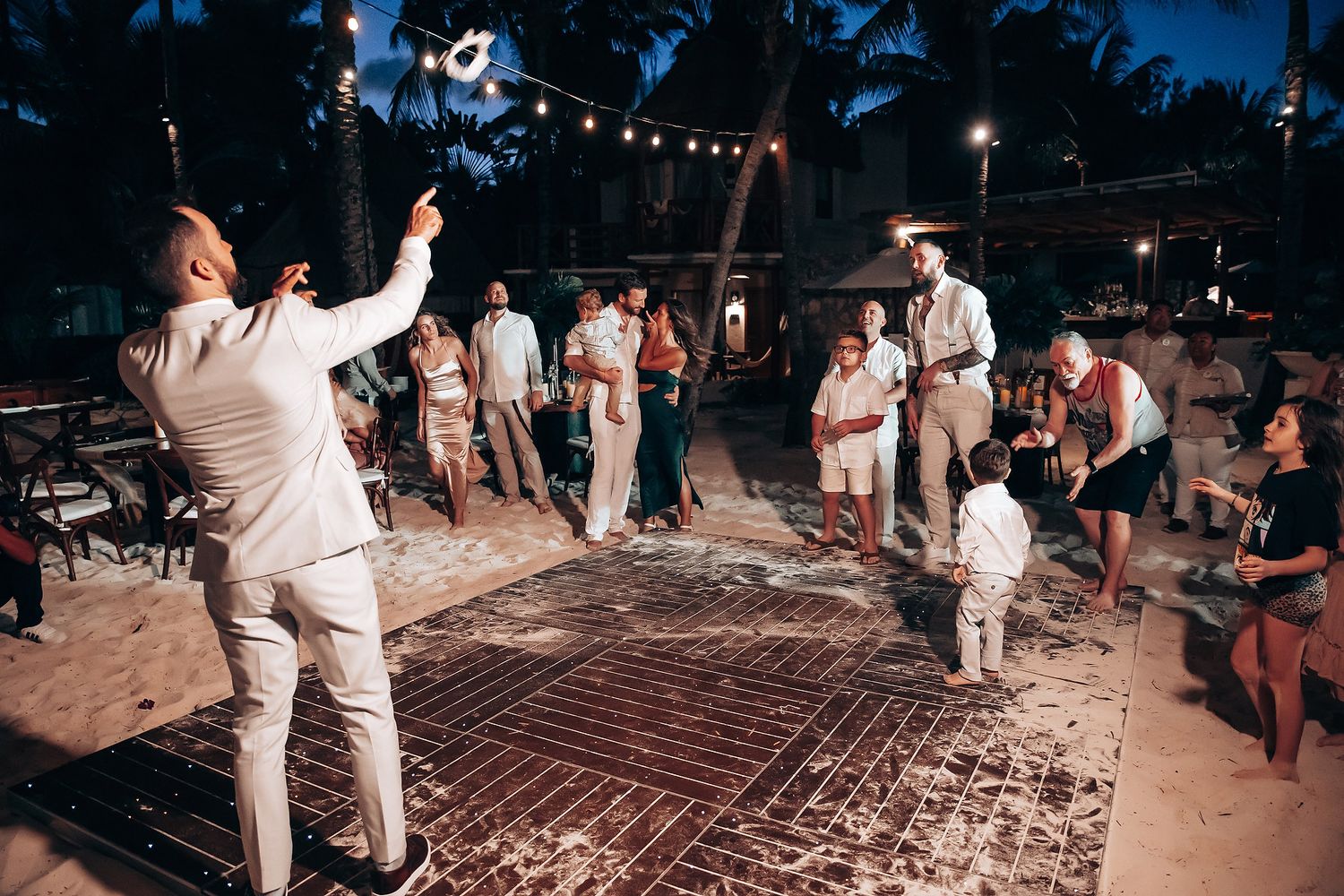 Wedding guests dancing on a wooden dance floor during an evening beach reception.