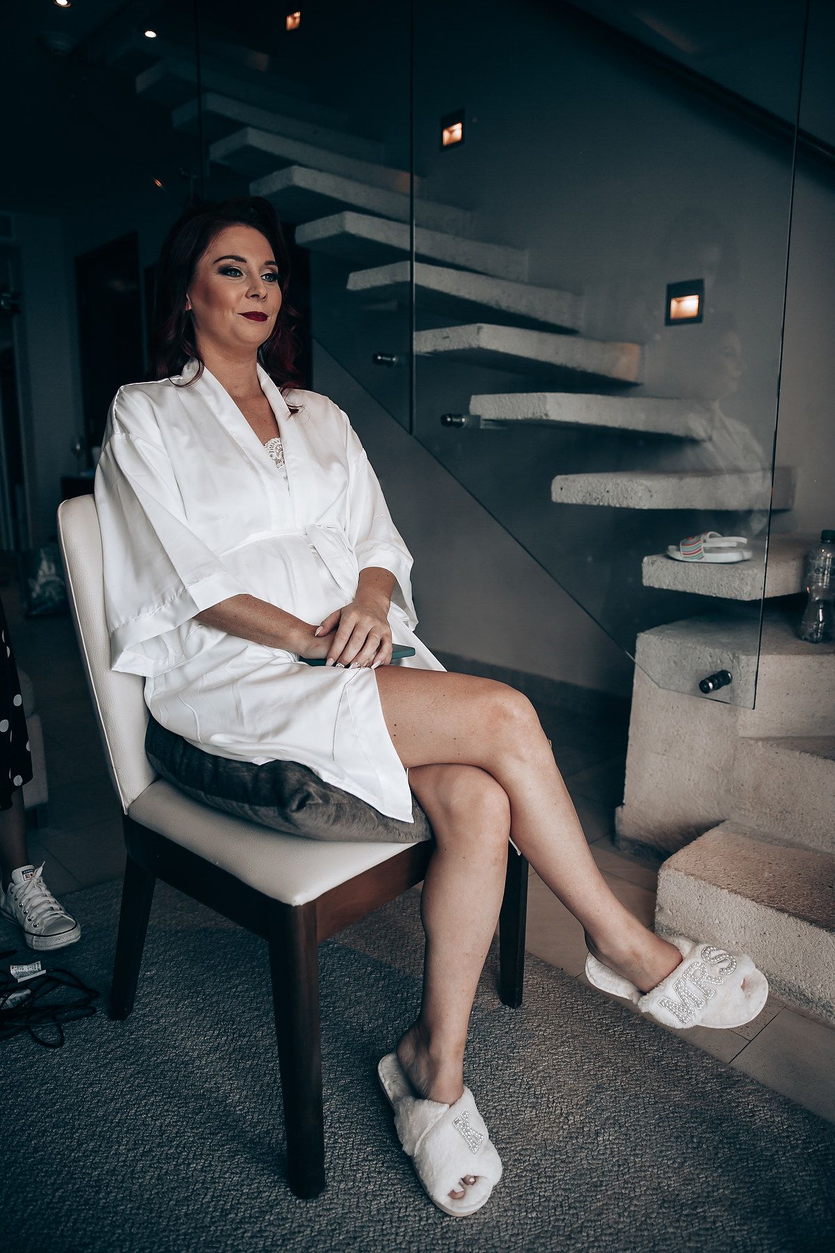 Multiple shots of someone in a white robe sitting on a modern chair with glass staircase in background.