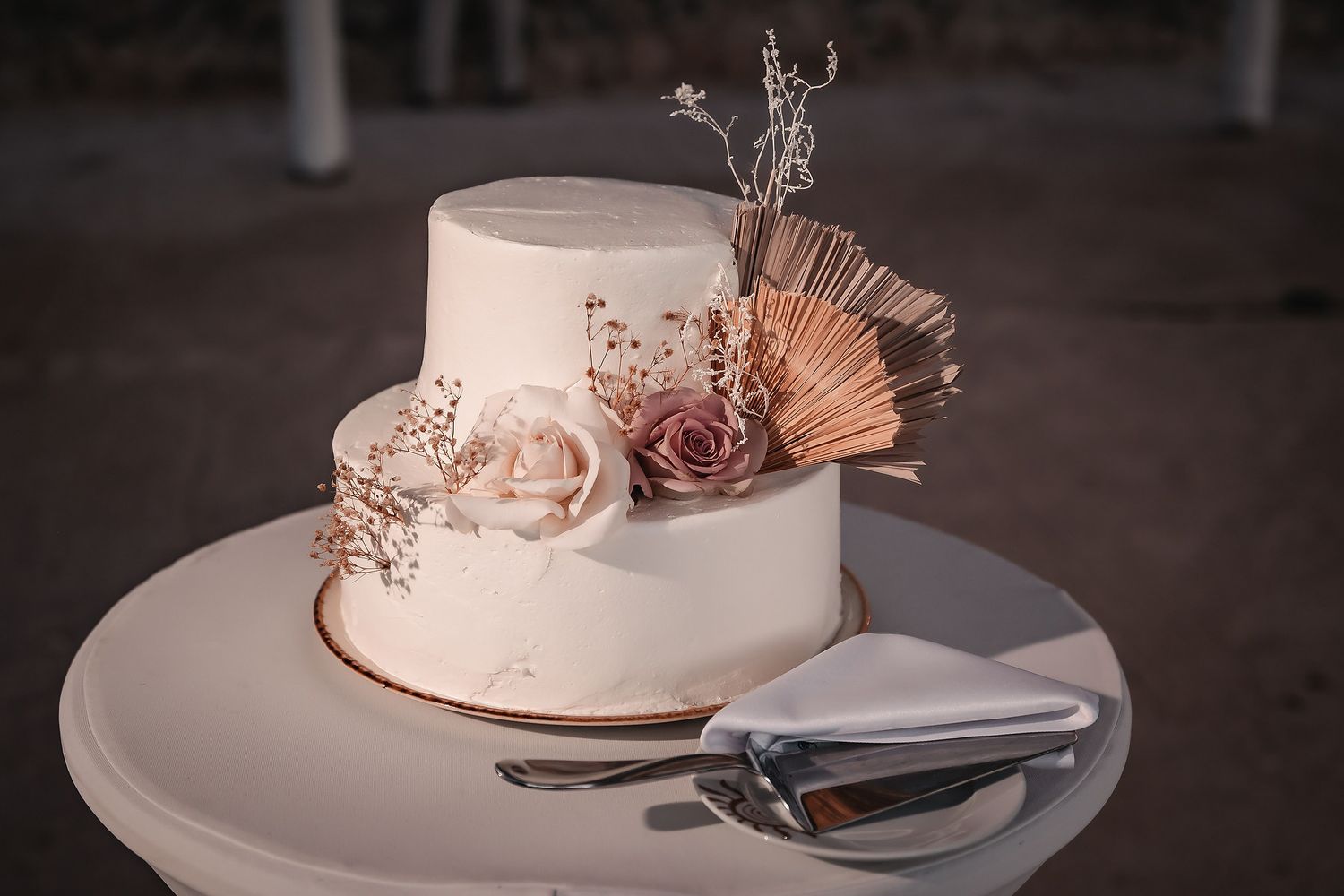 Elegant two-tier white wedding cake adorned with blush roses and dried flowers on a white cake stand.