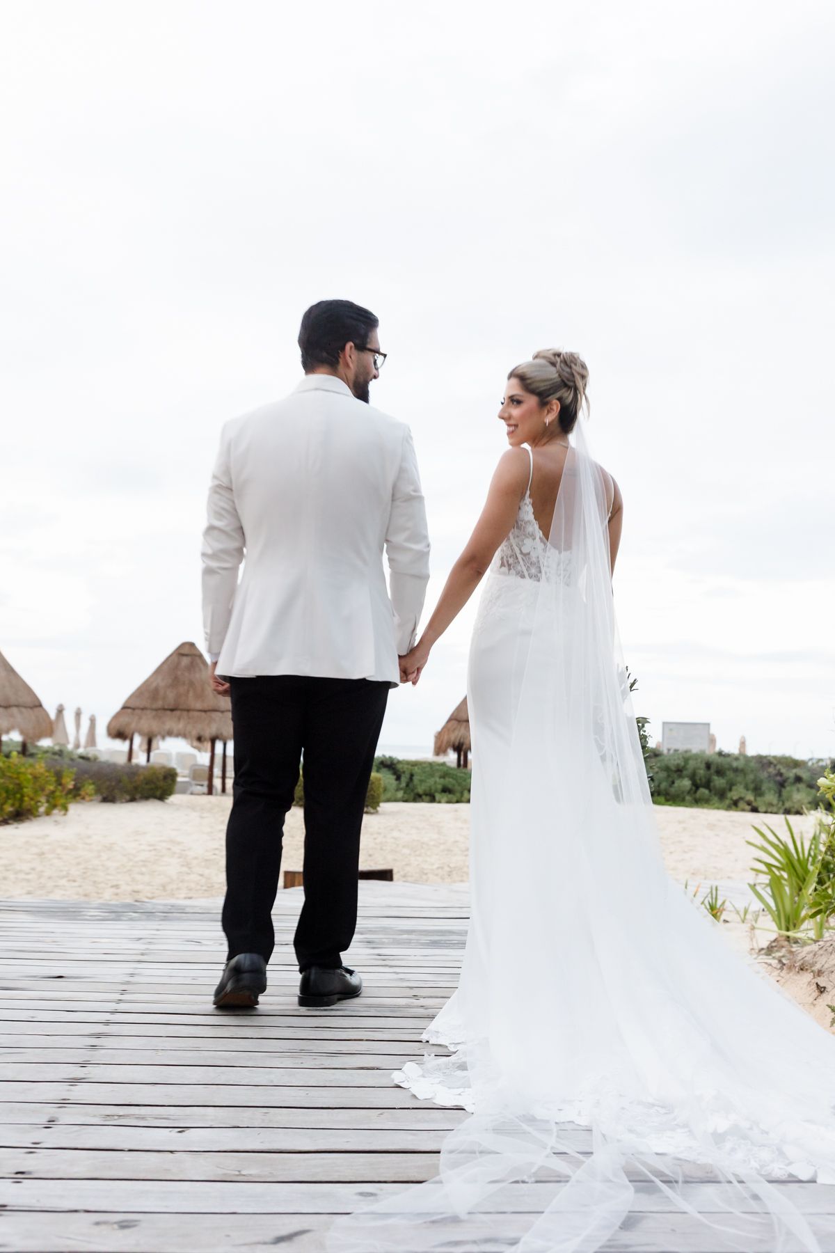 Bride and groom holding hands walking on a wooden boardwalk at a beach resort on their wedding day.