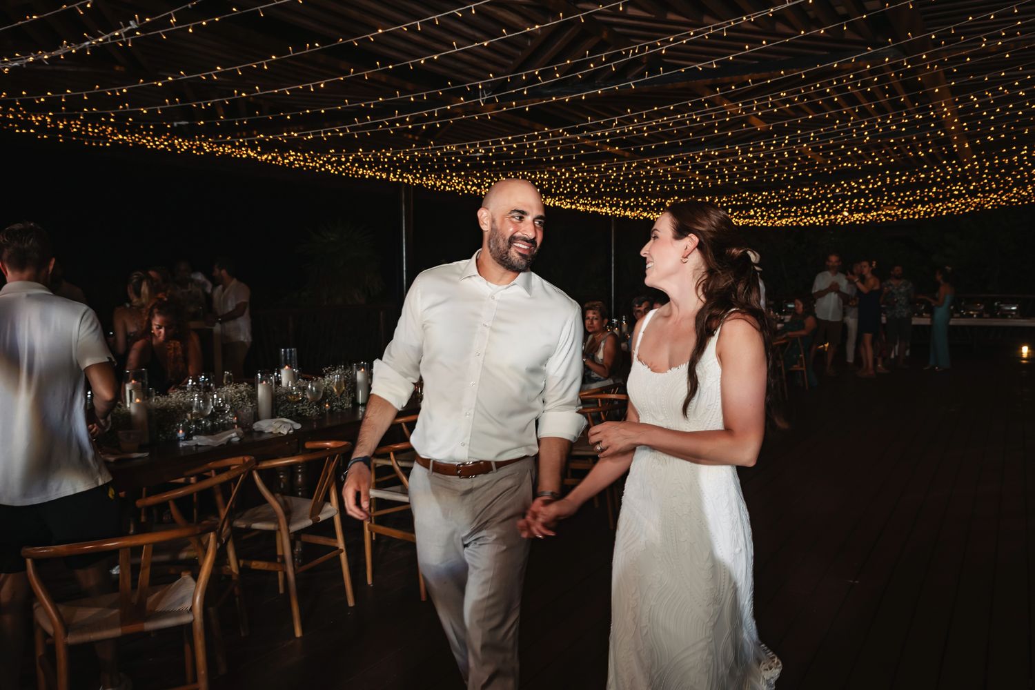 Couple dancing and smiling under string lights at an outdoor wedding reception at night.