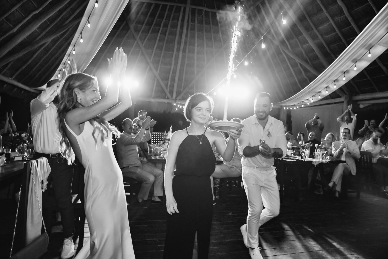 Bride and guests dance joyfully at a wedding reception under a decorated tent.