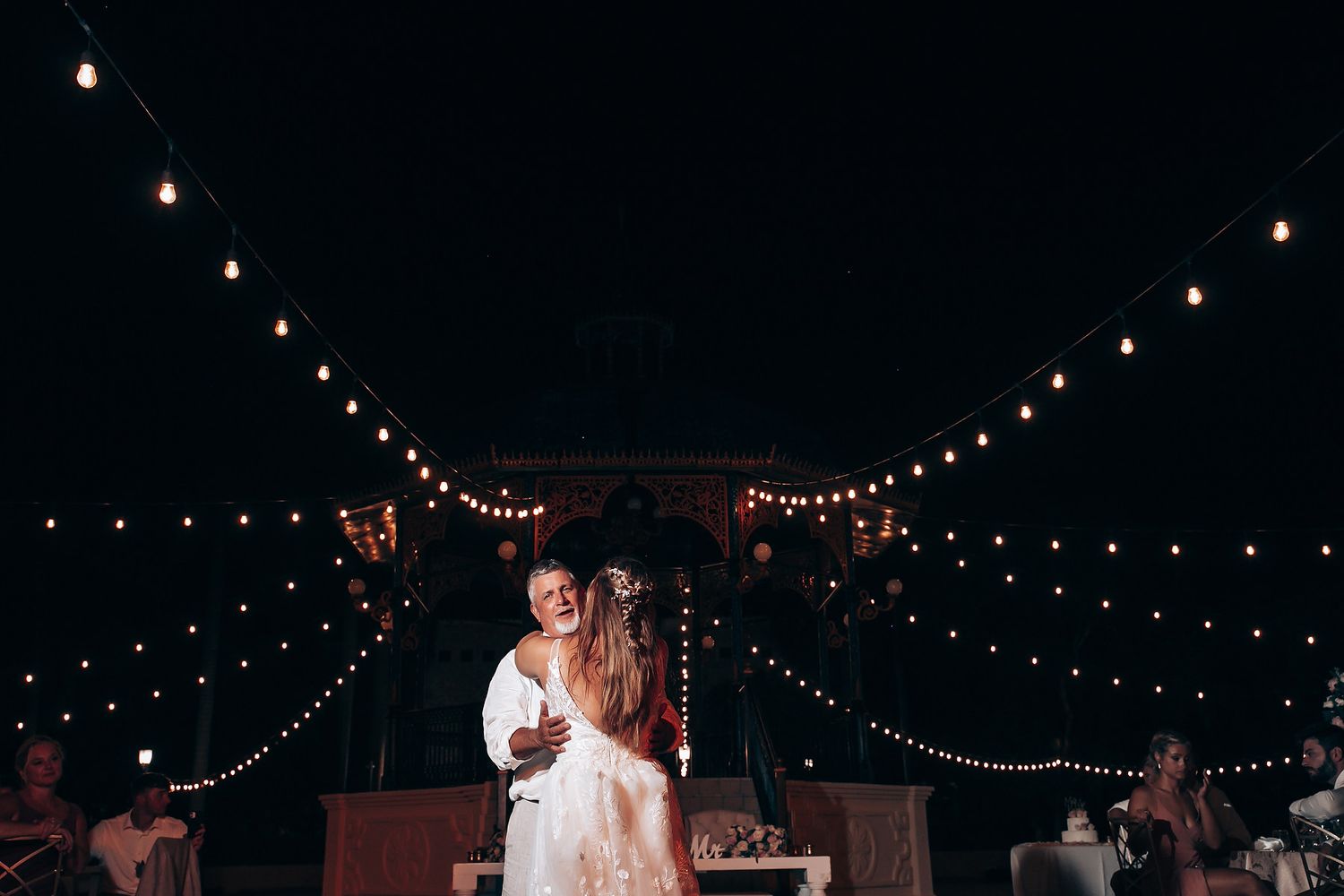 String lights create a magical canopy over an outdoor nighttime wedding celebration.