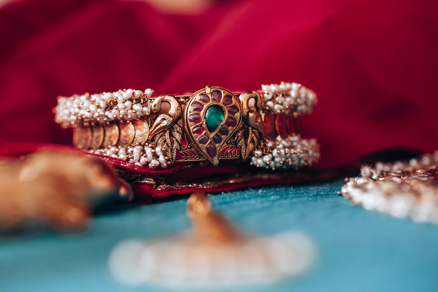 A collection of vintage-style rose gold and diamond rings with emerald accents displayed on a deep red velvet background.