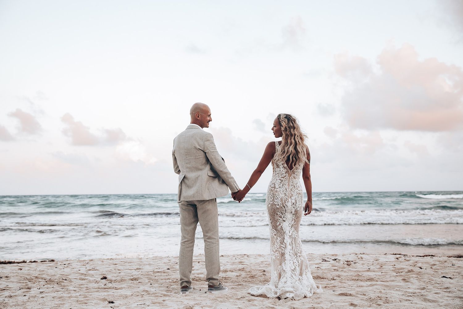 Couple walking hand in hand on a sandy beach at sunset with waves in the background.