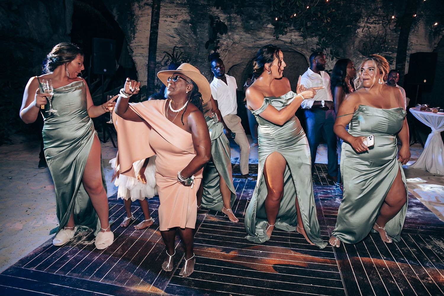 Wedding guests in sage green dresses dance energetically on the dance floor during reception.
