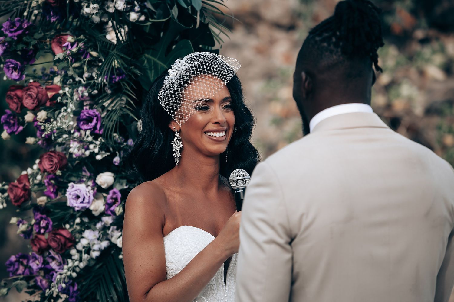 Intimate wedding moment captured under purple and pink floral arrangements.