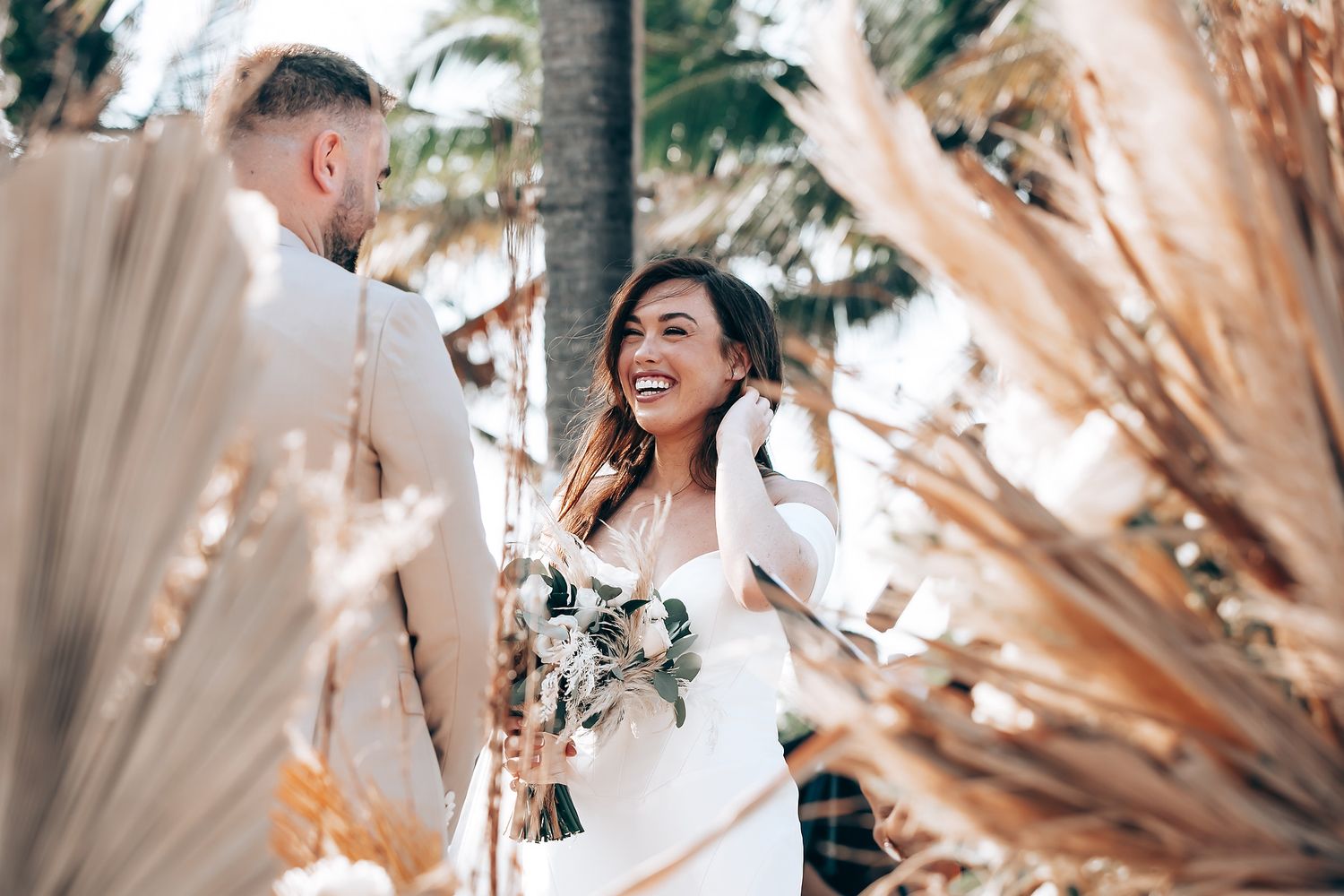 Wedding celebration at a beach venue with decorative dried pampas grass and natural sunlight.